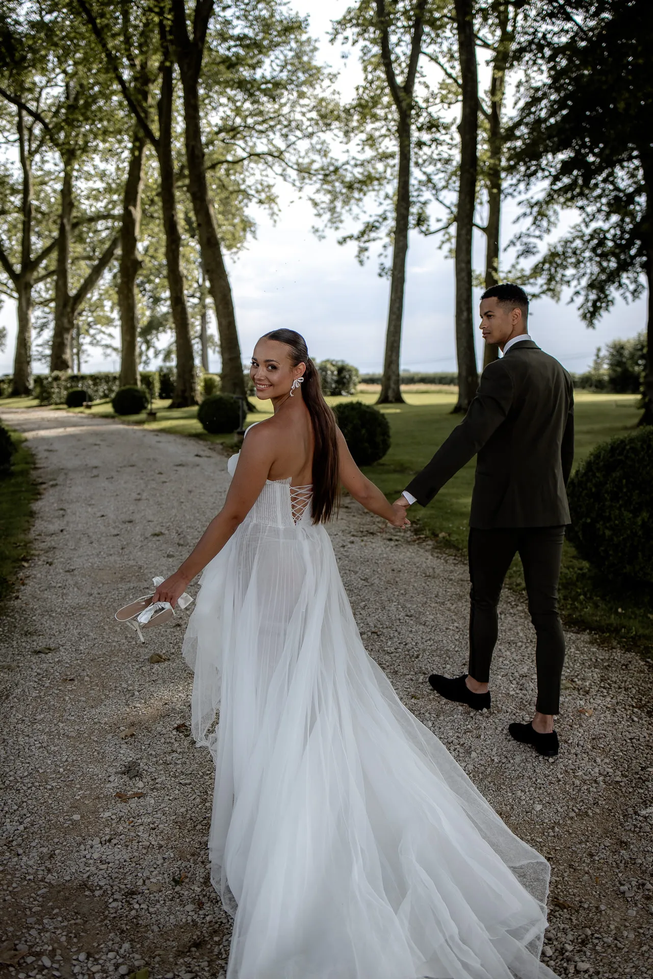 Glückliche Braut blickt zurück beim Paarshooting in der Baumallee des Chateau de Varennes Parks
